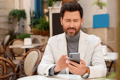 Handsome man sending message via smartphone at table outdoors
