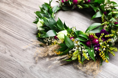 Photo of Beautiful wreath made of flowers and leaves on wooden table, closeup