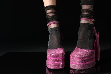 Photo of Woman wearing pink high heeled shoes with platform and square toes on black background, closeup. Space for text