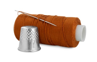 Photo of Thimble and spool of brown sewing thread with needle isolated on white