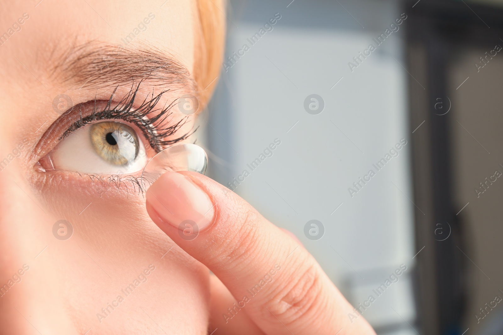 Photo of Young woman putting contact lens in her eye, closeup