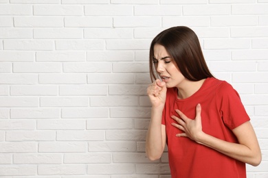 Photo of Beautiful young woman coughing near brick wall. Space for text