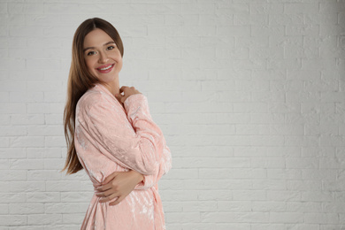 Beautiful young woman in bathrobe near white brick wall. Space for text