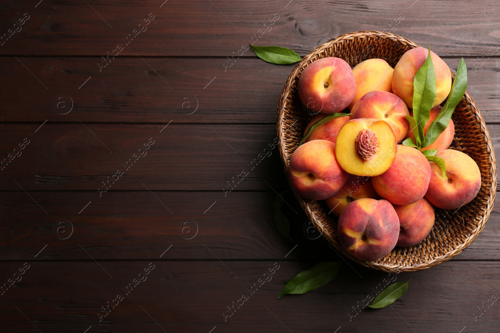 Photo of Fresh sweet peaches in wicker basket on wooden table, top view. Space for text