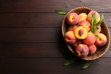 Photo of Fresh sweet peaches in wicker basket on wooden table, top view. Space for text