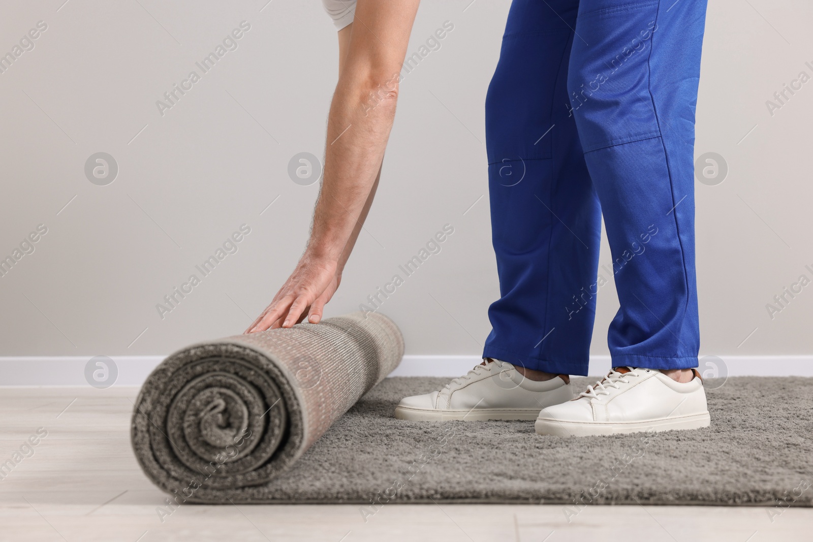 Photo of Worker unrolling new carpet on floor in room, closeup
