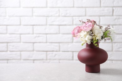 Photo of Beautiful bouquet with roses on light table against white brick wall, space for text
