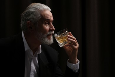 Photo of Senior man in suit drinking whiskey on black background