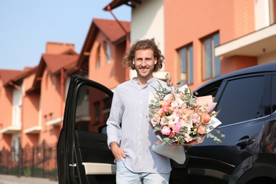 Young handsome man with beautiful flower bouquet near car on street