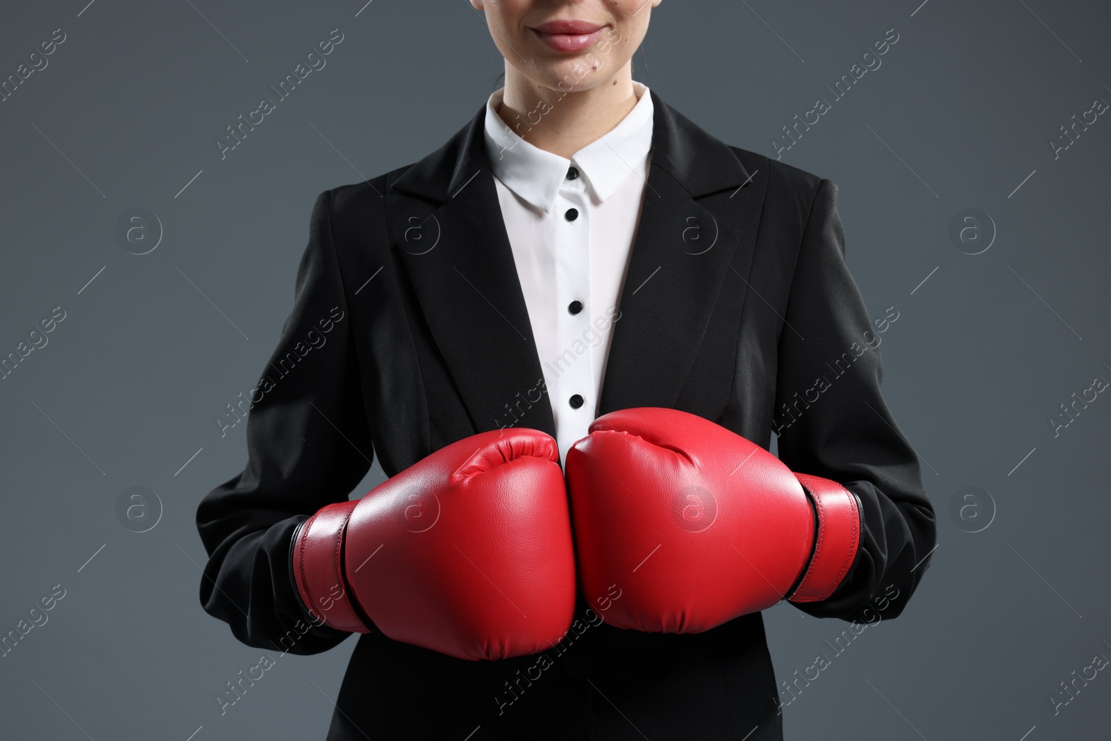 Photo of Businesswoman in suit wearing boxing gloves on grey background, closeup