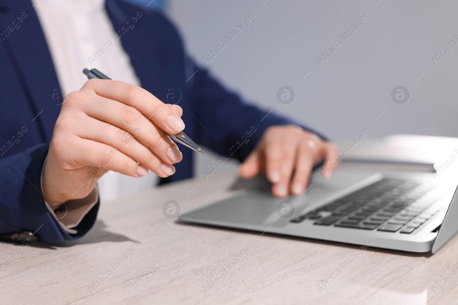 Photo of Woman with pen working on laptop at wooden table, closeup. Electronic document management