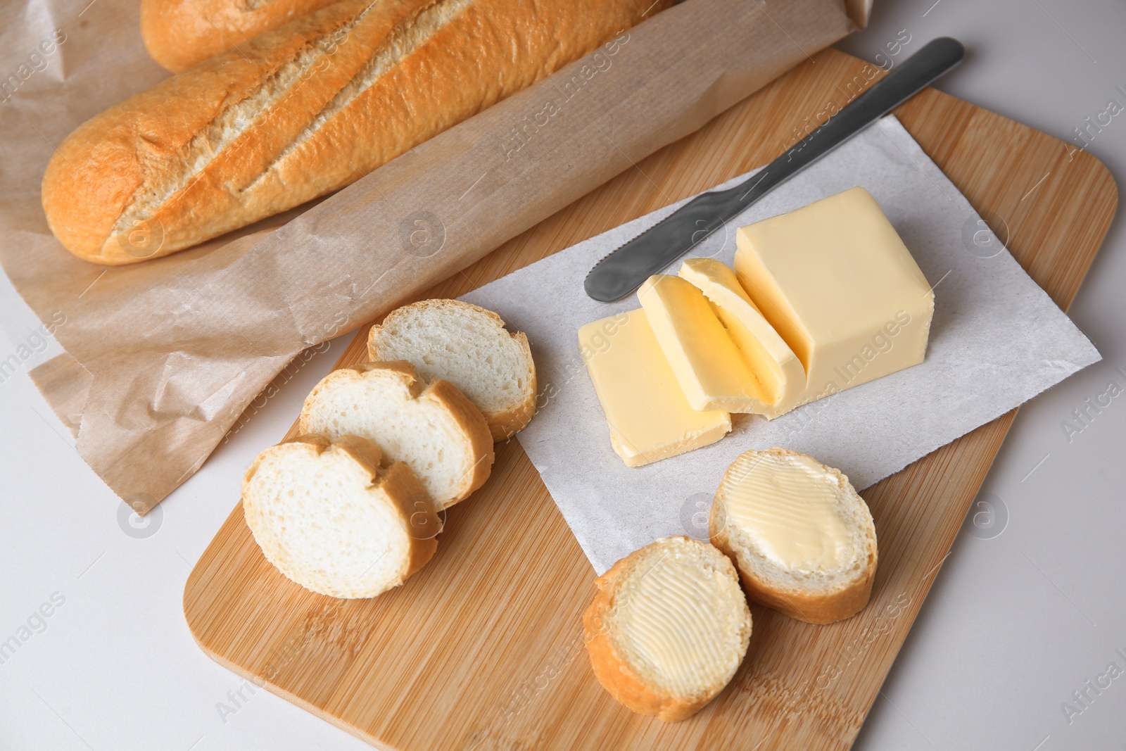 Photo of Tasty cut baguette with fresh butter on white table