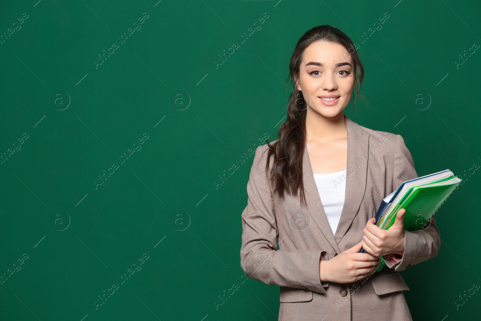 Photo of Portrait of beautiful young teacher with books near chalkboard, space for text