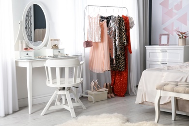 Rack with collection of beautiful festive clothes and dressing table in stylish bedroom interior