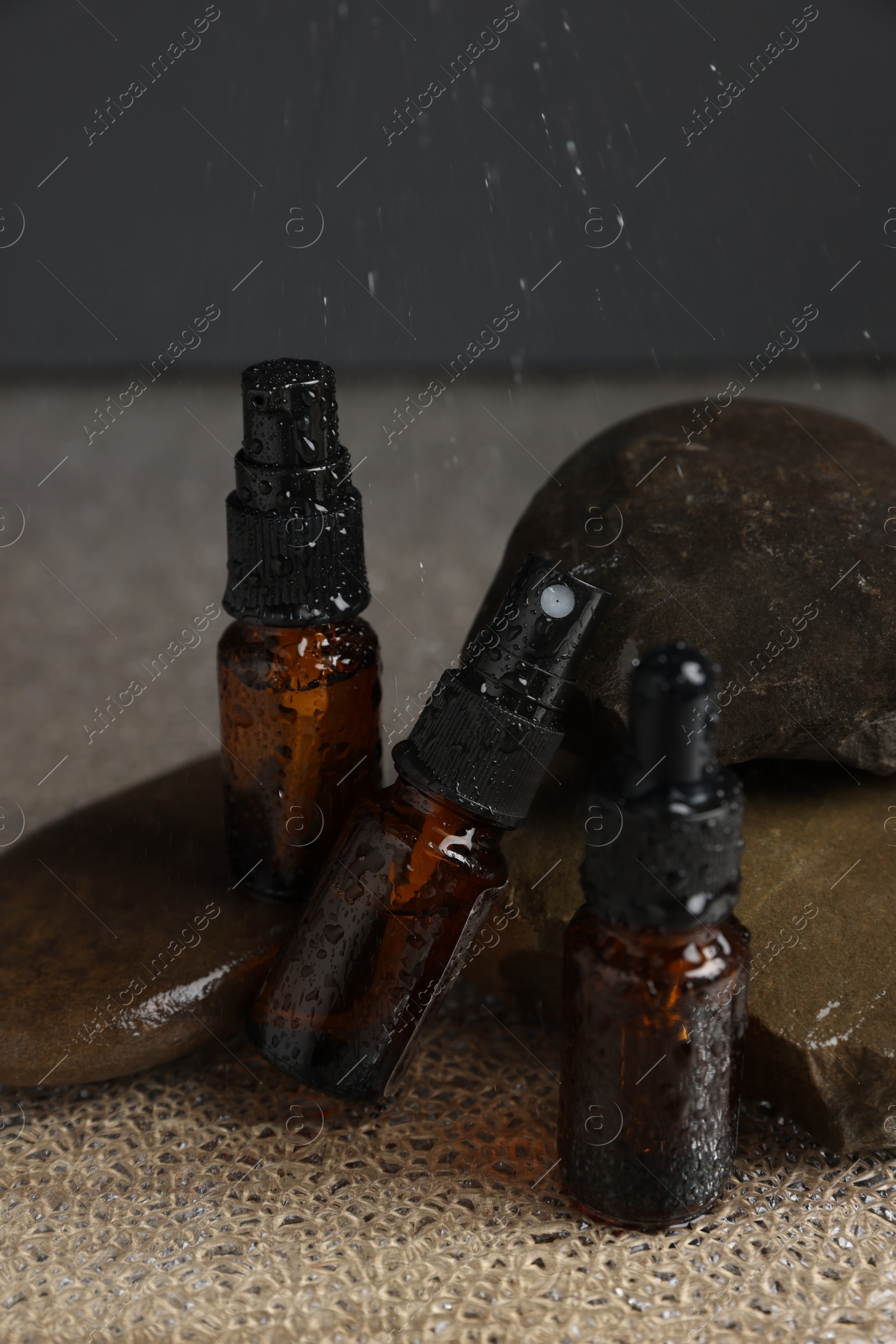 Photo of Bottles of organic cosmetic products and stones on wet surface