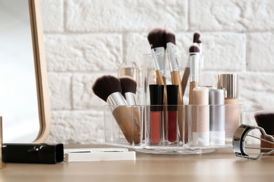 Photo of Organizer with cosmetic products for makeup on table near brick wall