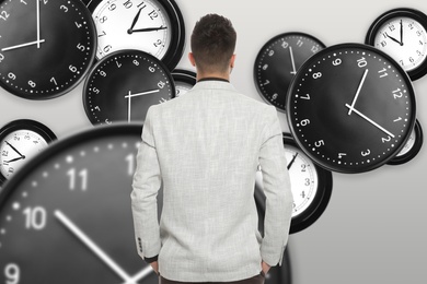 Image of Time management concept. Businessman standing in front of different clocks on light background, back view