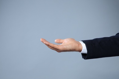 Photo of Businessman holding something on grey background, closeup view of hand with space for text