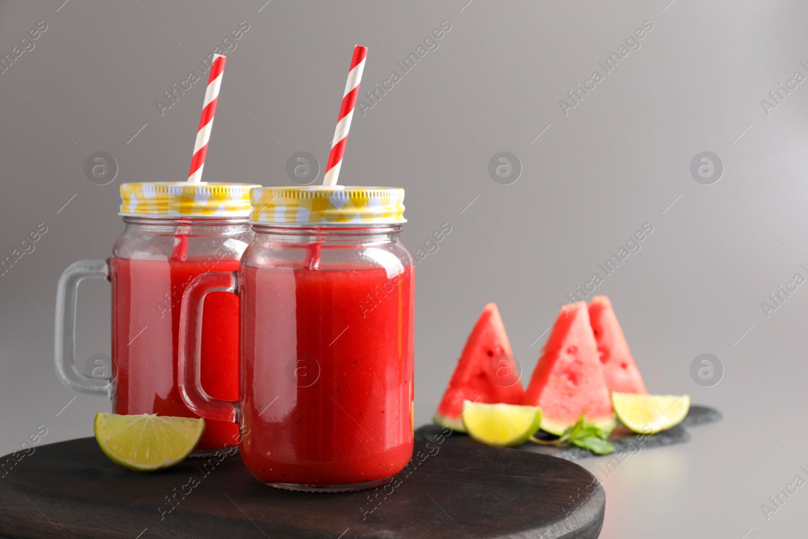 Photo of Tasty summer watermelon drink with lime in glass mason jars on grey background. Space for text