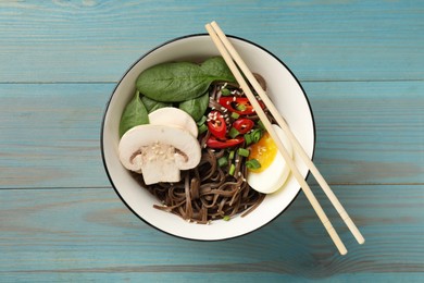 Photo of Tasty buckwheat noodles (soba) with chili pepper, egg, mushrooms and chopsticks on light blue wooden table, top view