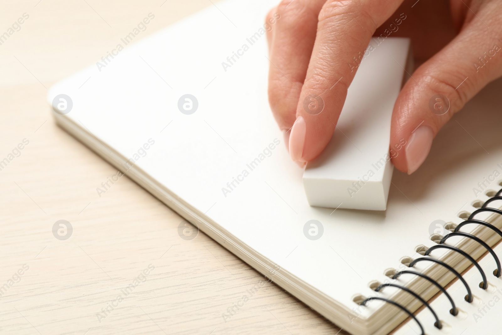 Photo of Woman erasing something in notebook at wooden table, closeup