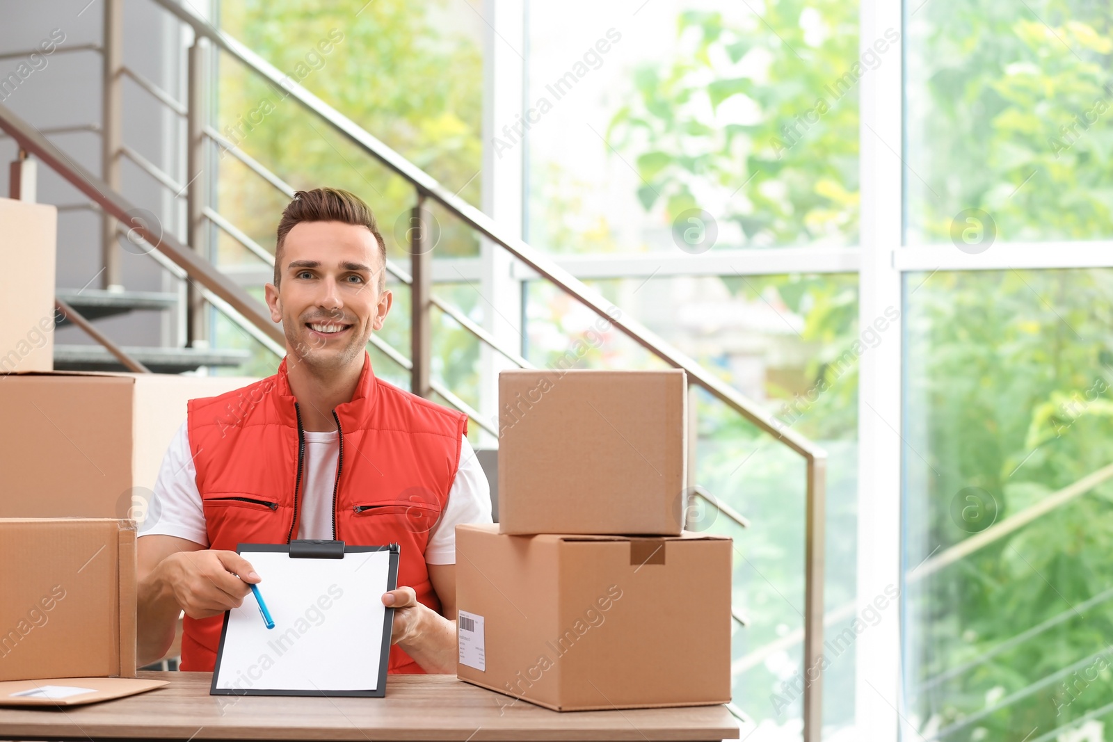 Photo of Young courier with clipboard among parcels at delivery department. Space for text