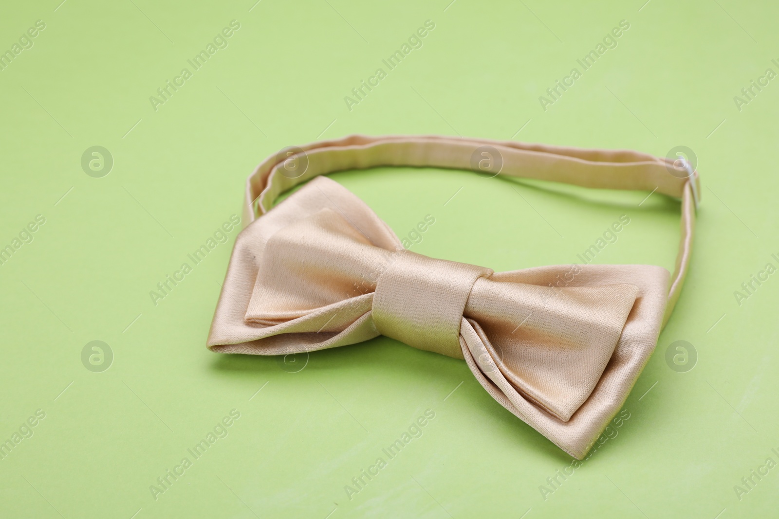 Photo of Stylish beige bow tie on light green background, closeup