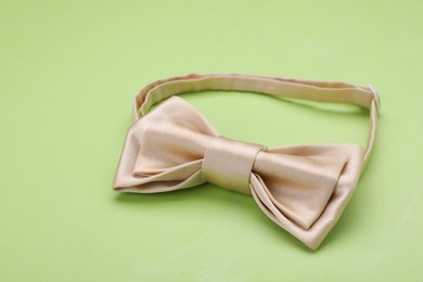 Stylish beige bow tie on light green background, closeup