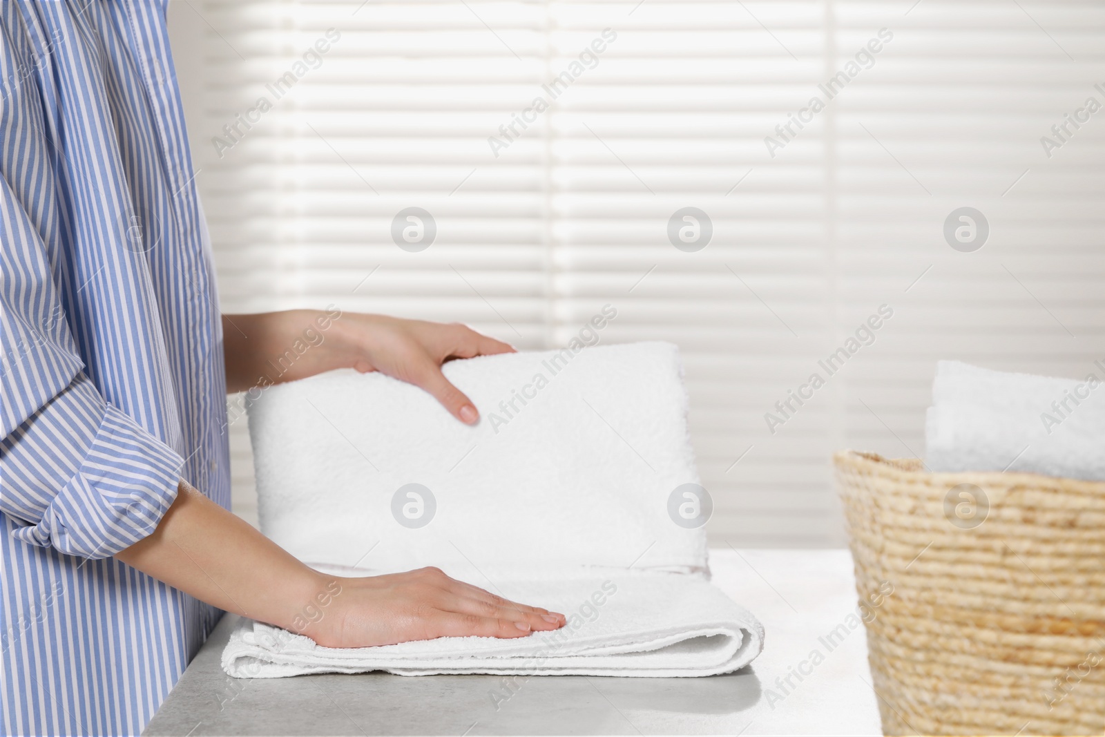 Photo of Woman folding clean terry towel at table indoors, closeup