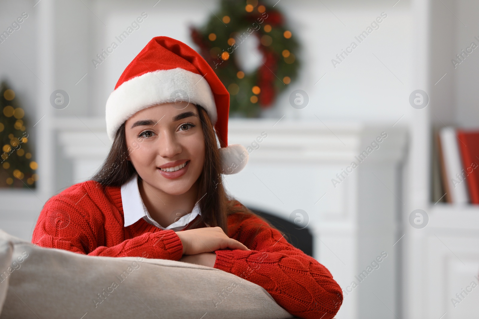 Photo of Portrait of smiling woman wearing red Christmas hat in cosy room. Space for text