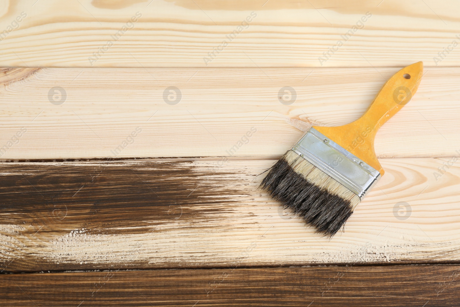 Photo of Brush with wood stain on wooden surface. Space for text