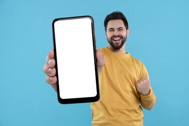 Happy man holding smartphone with empty screen on light blue background