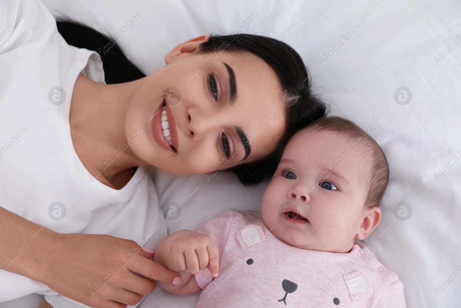 Photo of Young mother with her little baby on bed, top view