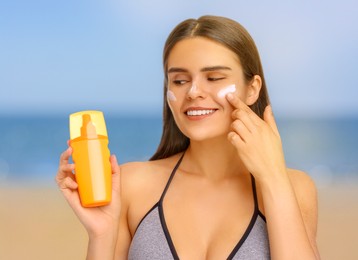 Image of Sun protection. Beautiful young woman applying sunblock onto face on beach