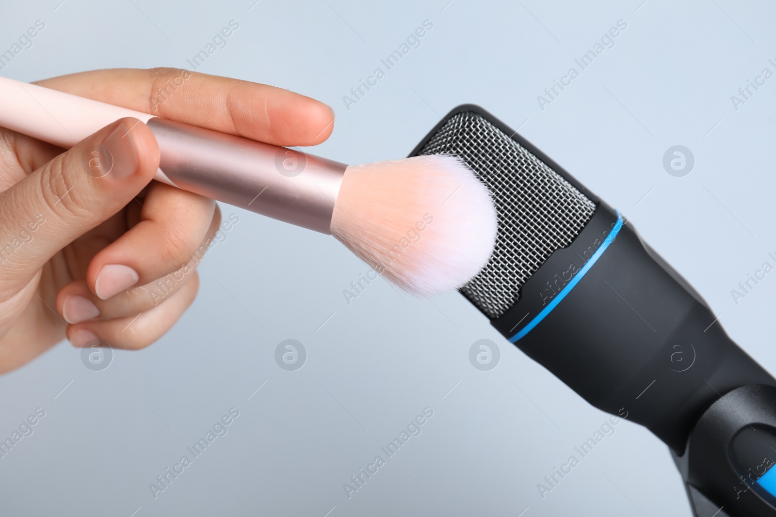Photo of Woman making ASMR sounds with microphone and brush on grey background, closeup