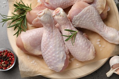 Wooden board with fresh raw chicken legs and other products on grey table, top view