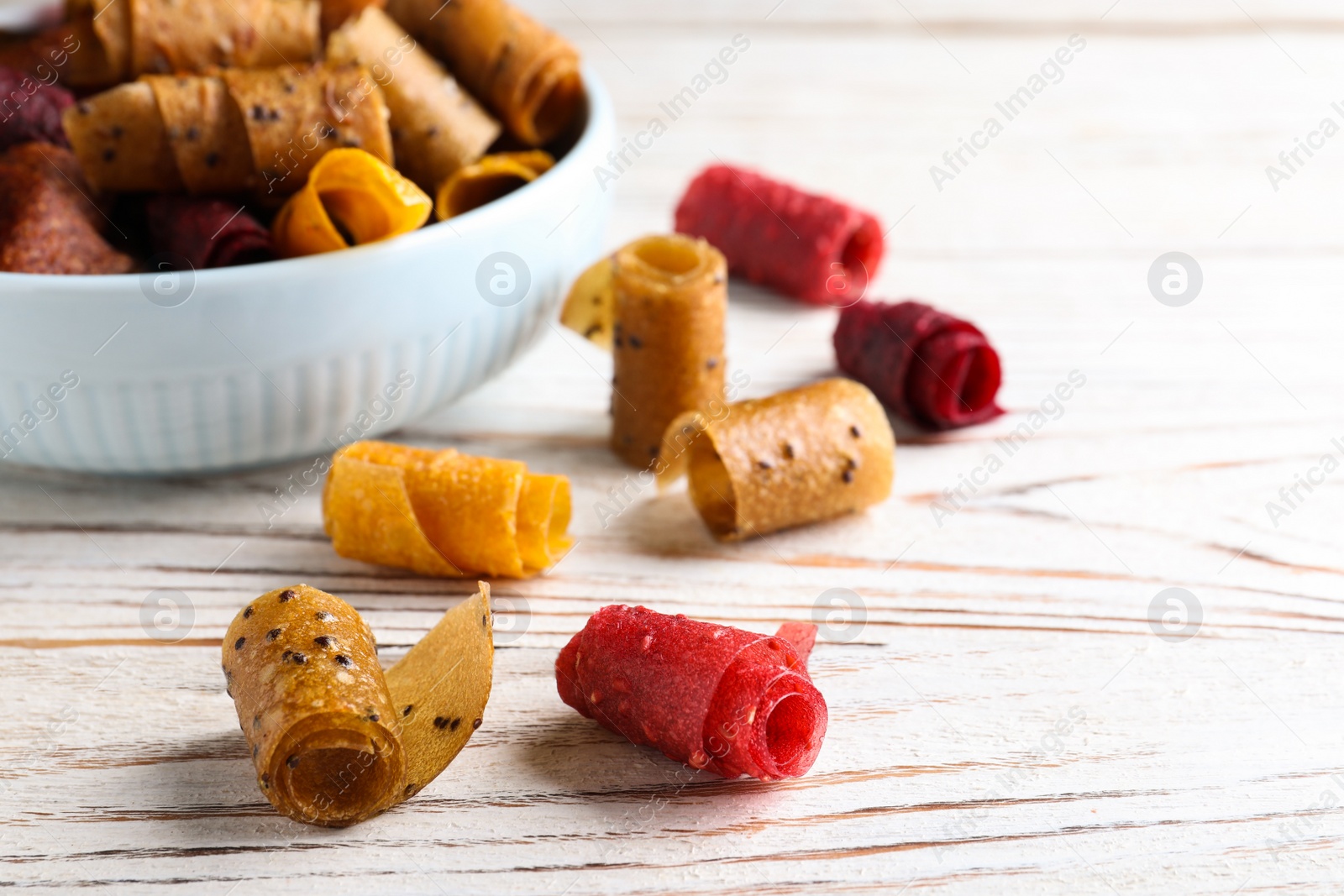 Photo of Delicious fruit leather rolls on white wooden table, closeup