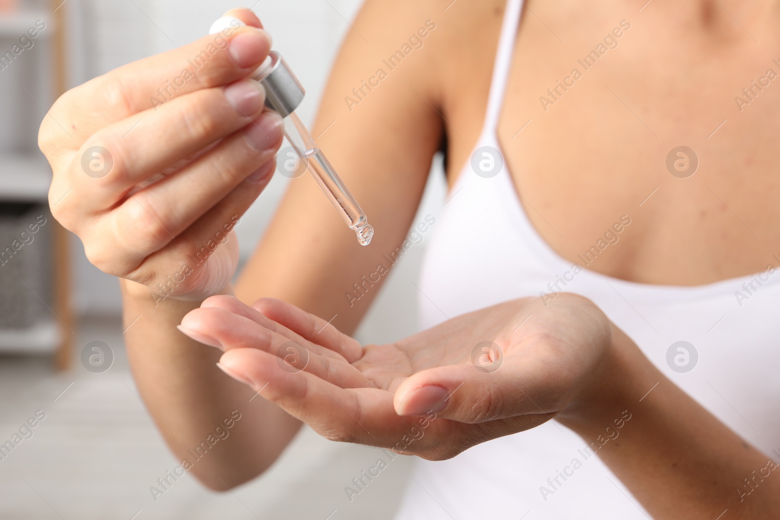 Photo of Woman applying cosmetic serum onto her hand on blurred background, closeup