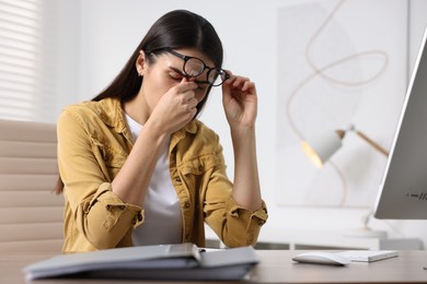 Young woman suffering from headache at wooden table in office