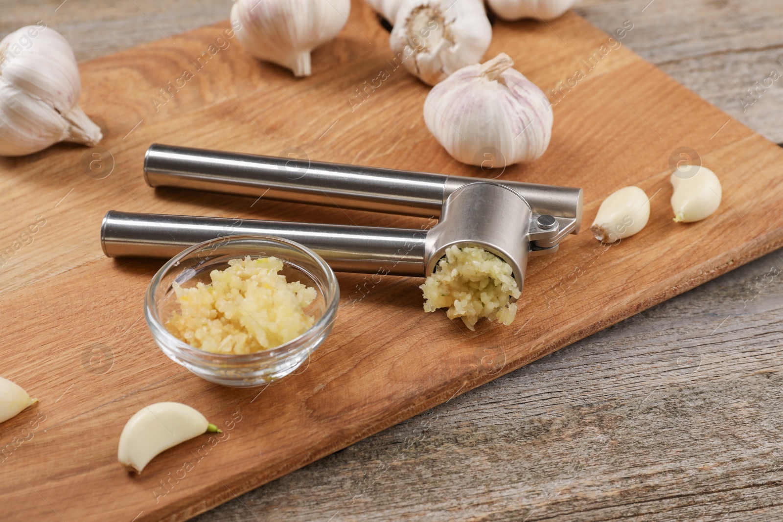 Photo of Garlic press, cloves and mince on wooden table. Kitchen utensil