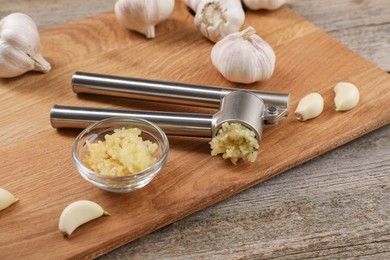 Garlic press, cloves and mince on wooden table. Kitchen utensil