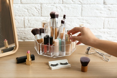 Woman taking cosmetics from organizer for makeup products on table