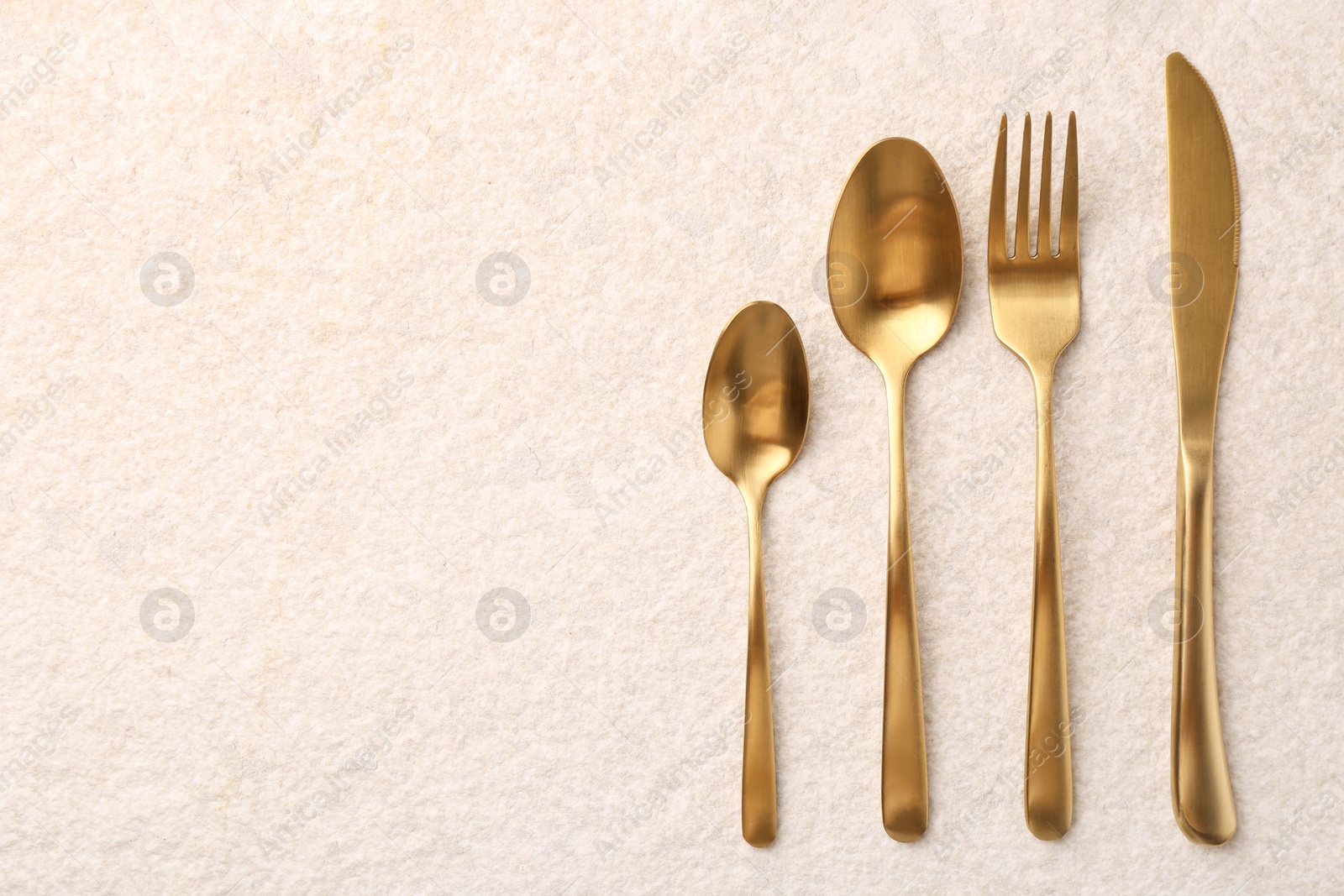 Photo of Stylish golden cutlery set on light textured table, flat lay. Space for text