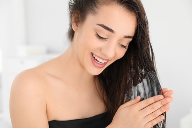 Beautiful young woman applying hair conditioner in bathroom