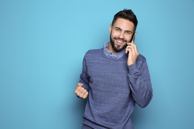 Photo of Happy young man with smartphone celebrating victory on color background. Space for text