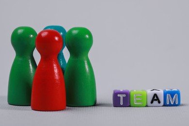 Photo of Colorful pawns and cubes with word Team on light grey background, closeup. Recruiter searching employee