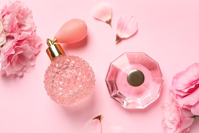 Flat lay composition with perfume bottles and flowers on light pink background