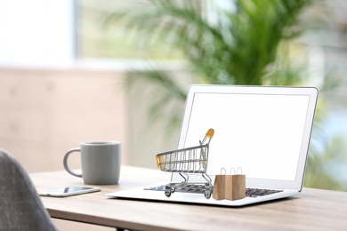 Image of Online shopping. Modern laptop with small cart and bags on table