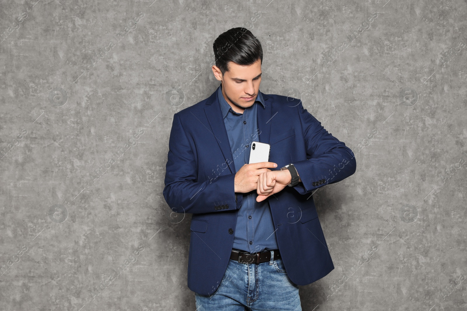 Photo of Portrait of businessman with mobile phone looking at wristwatch on grey background