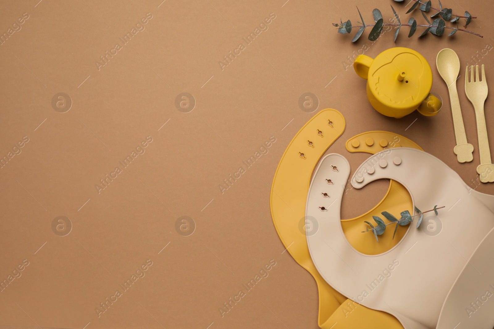 Photo of Flat lay composition with baby feeding accessories and bibs on brown background, space for text